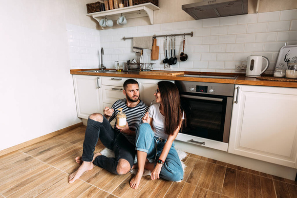 Young man and woman sitting on floor in kitchen and talking. Loving young couple spending time together at home. Happy family. A happy couple at home. Couple in love in the kitchen. - Fotografie, Obrázek