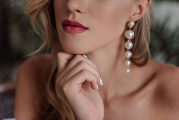 A beautiful girl with natural, beautiful, professional makeup and a fancy fashion fashion cut in her hair and long white pearl earrings. hands near the face, a large portrait. selective focus - Foto, Imagem