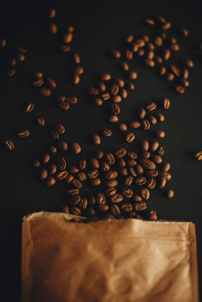 黒の背景に紙パックから散乱コーヒー豆フラットレイ。新鮮な香り高いローストコーヒー豆の上からの眺め。コーヒーショップのコンセプト。暗いムーディ画像 - 写真・画像