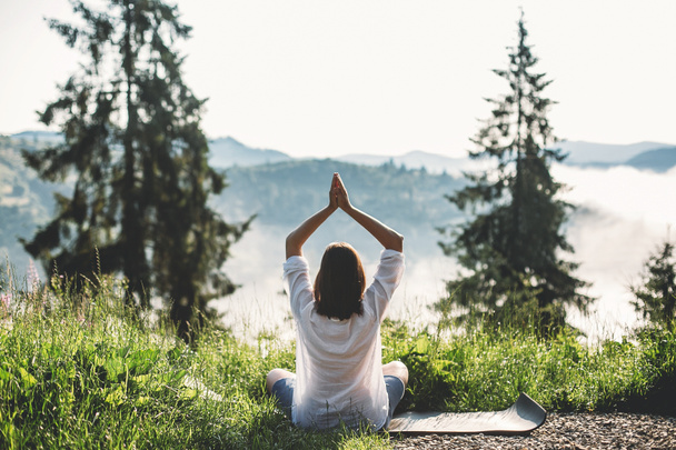 Молодая женщина практикует йогу и сидит среди травы в солнечном свете на фоне утренних гор. Медитация. Спокойный момент, связь с природой. Копирование пространства
 - Фото, изображение