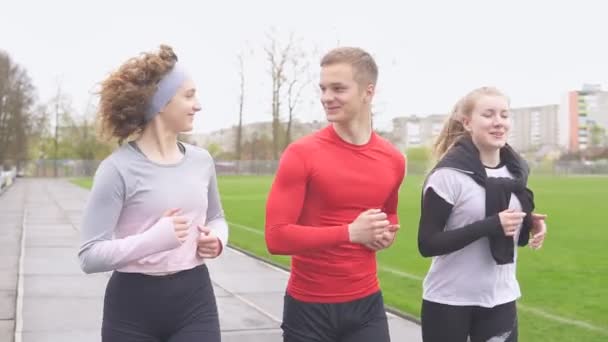 Skupina dospívajících sportovních přátel běží společně na stadionu a usmívá - Záběry, video