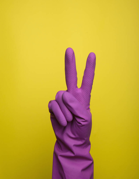 Hand with yellow rubber protective glove isolated on pink gesturing two 2. Signs of gestures (language), gloves cleaning, kitchen gloves. - Photo, Image