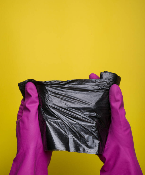  Μαύρο δοχείο σκουπιδιών, σκουπιδοτενεκές. Σακούλα αποβλήτων. γενική ή τακτική καθαρισμό. Εμπορική έννοια εταιρεία καθαρισμού. προϊόντα απολύμανσης. Εξυγιαντικό. πολύχρωμα γάντια σε κίτρινο φόντο - Φωτογραφία, εικόνα