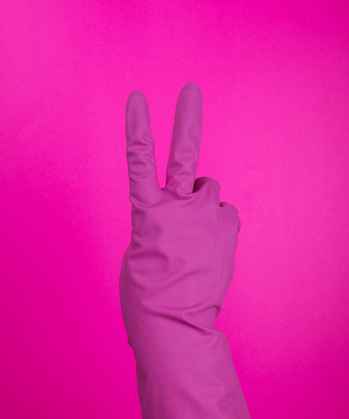 Мбаппе с желтой резиновой защитной перчаткой, изолированной на розовой жестикулирующей двойке. Признаки жестов (языка), перчаток уборки, кухонных перчаток. - Фото, изображение