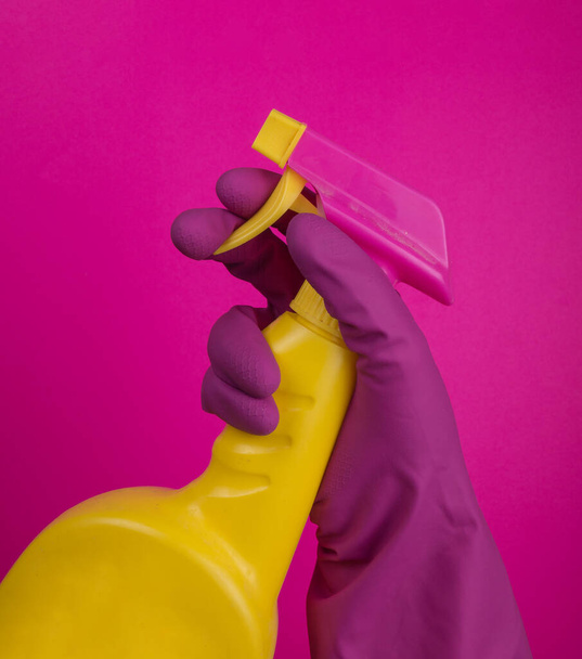Ręka czyściciela wfioletowej gumowej rękawicy ochronnej trzymającej chemiczną butelkę natryskową. Puste miejsce na tekst lub logo na szarym tle. Wczesna wiosna lub regularne sprzątanie. Przedsiębiorstwo sprzątające  - Zdjęcie, obraz