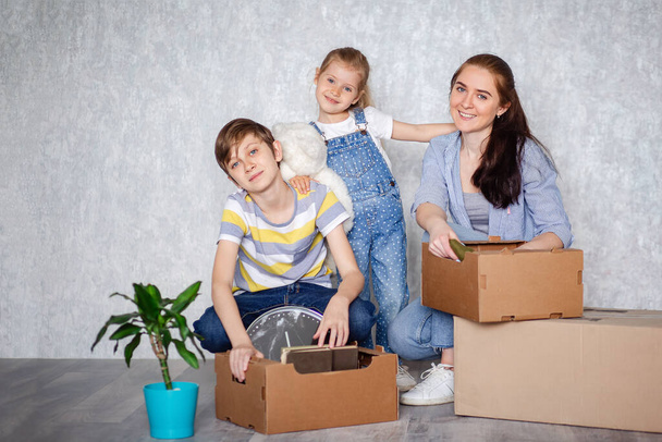 Een moeder met haar zoon en dochter verhuist naar een nieuw appartement met spullen in kartonnen dozen. Het gezin creëert een dak dat een uitstekende bescherming voor kinderen belooft - Foto, afbeelding
