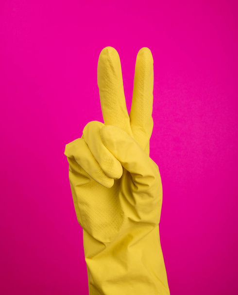 Mano con guante de goma amarilla aislado sobre gestación rosa dos 2. Signos de gestos (lenguaje), limpieza de guantes, guantes de cocina.. - Foto, Imagen
