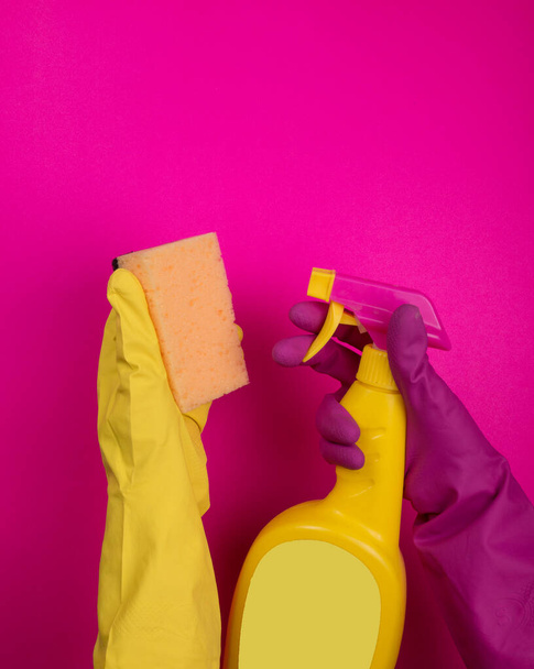 Hand in Hand hält ein farbiger Gummihandschuh einen Reinigungsschwamm auf buntem Hintergrund. Reinigungskonzept, Reinigungsservice. Banner. Flache Lage, Draufsicht. Reinigungsmittel - Flaschen, Sprays. Schwamm - Foto, Bild