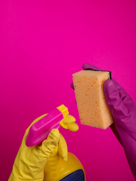 Hand in Hand hält ein farbiger Gummihandschuh einen Reinigungsschwamm auf buntem Hintergrund. Reinigungskonzept, Reinigungsservice. Banner. Flache Lage, Draufsicht. Reinigungsmittel - Flaschen, Sprays. Schwamm - Foto, Bild