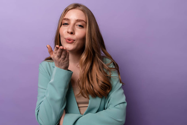 Image of pleased happy woman posing indoors isolated over purple wall background blowing kisses. - Foto, Imagen