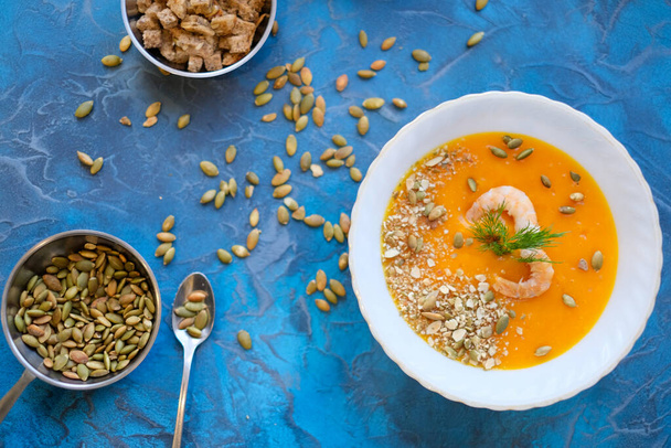 pumpkin soup in women hands with purple Basil on a blue background. Top View, sunflower seeds, green onions and prawns, purple basil in a serving bowl on a blue background. - Foto, Bild