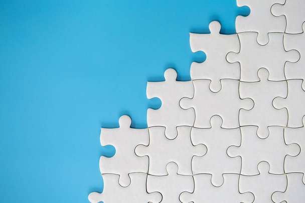 White jigsaw puzzle pieces on a blue background. Problem solving concepts. Texture photo with copy space for text - Photo, Image
