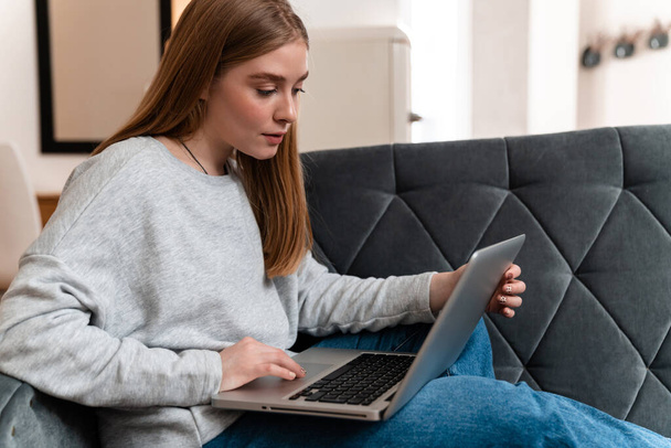 Photo of a concentrated beautiful young woman indoors at home on sofa using laptop computer. - Fotoğraf, Görsel