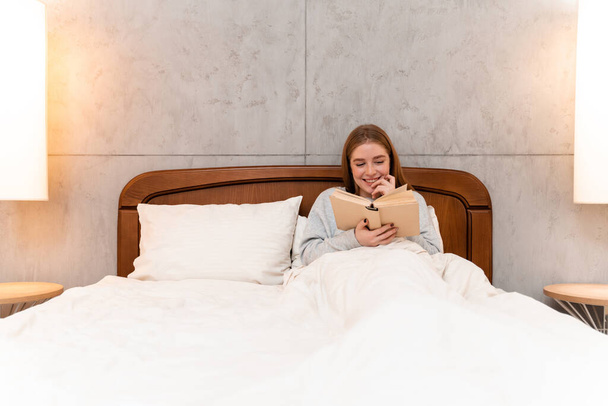 Photo of a positive happy beautiful young woman indoors at home in bed reading book. - Fotoğraf, Görsel