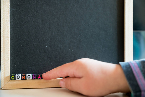 Kind schrijven CORONA met behulp van alfabet kralen op zwart bord. - Foto, afbeelding