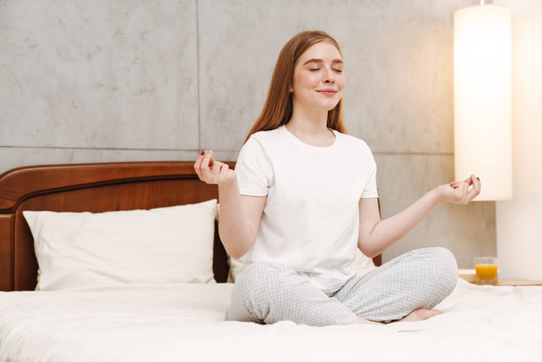 Image of young cute pleased girl indoors at home in bedroom meditate on bed. - Foto, immagini