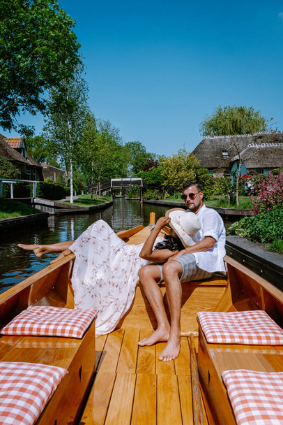 Giethoorn Niederlande Paar besucht das Dorf mit einem Boot, Blick auf das berühmte Dorf mit Kanälen und rustikalen Reetdachhäusern in landwirtschaftlicher Umgebung an einem heißen Frühlingstag - Foto, Bild