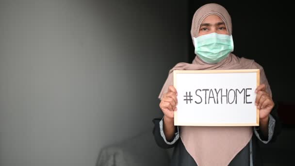 Mladá krásná muslimka v lékařské masce, při pohledu na kameru a ukázat kresbu "# STAYHOME" k prevenci nemocí a prachu, pm.5, Zůstaňte doma v karanténě koronavirus pandemické prevence. Kopírovat prostor. - Záběry, video