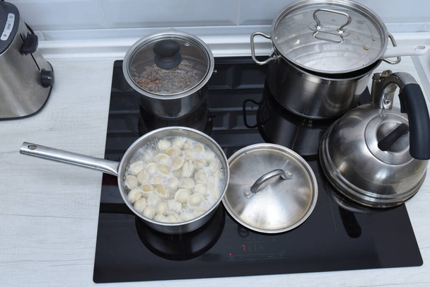 Ravioli in pan, kokend water, zilver metalen achtergrond. Koken Pelmeni, russische knoedels gevuld met gehakt, in stalen stoofpot op keramische kookplaat in de huiskeuken. Varenyky, vareniki. - Foto, afbeelding