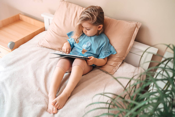 Beautiful child little girl playing with a tablet while lying on bed at home.  - Foto, imagen