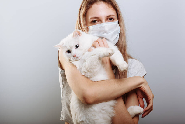 Sexy lady in protective surgical mask holds cat pet in face mask. Chinese Coronavirus disease COVID-19 is dangerous for pets. - Photo, Image