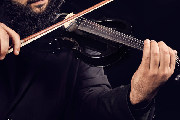 Muzikant die een stuk muziek speelt met een zwarte viool op een zwarte achtergrond - Foto, afbeelding