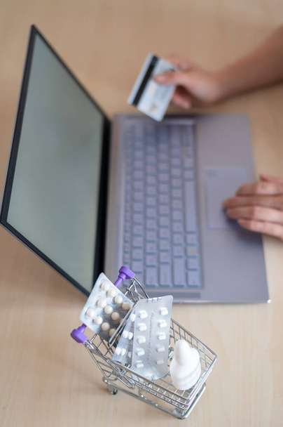 Online pharmacy concept. A woman holds a bank card in her hands and buys pills online. A girl makes an online purchase of pharmaceuticals with home delivery on a laptop. - Foto, Imagem