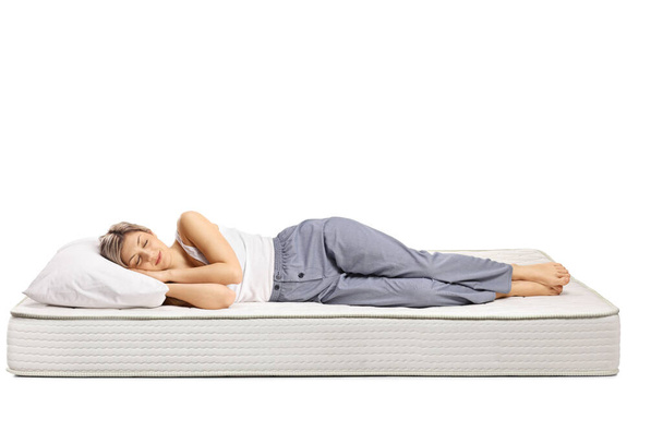 Young woman in pajamas sleeping on a comfortable mattress isolated on white background - Fotó, kép