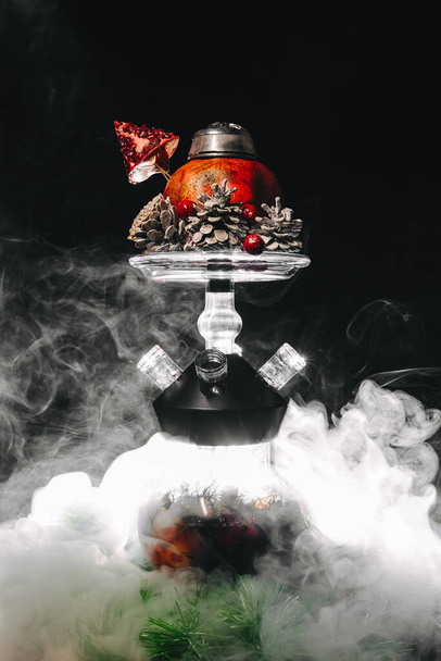 Festive xmas pomegranate hookah with frosted cones on black background, with swirling smoke around - Photo, image