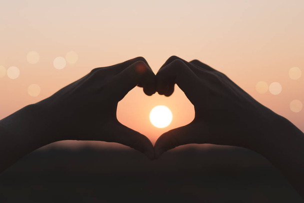 Женщина руки сделать форму сердца на закате неба и bokeh фона. - Фото, изображение