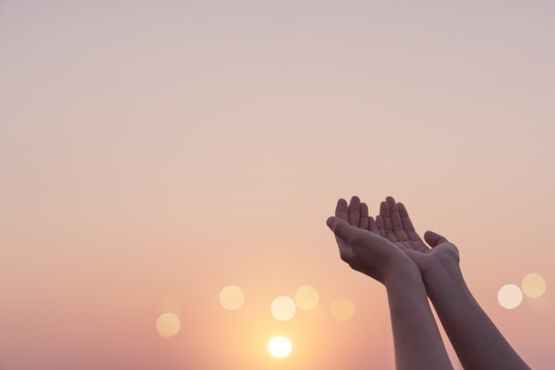 Γυναίκα χέρια τόπο μαζί, όπως προσεύχεται μπροστά από τη φύση θόλωμα παραλία ηλιοβασίλεμα ουρανό φόντο. - Φωτογραφία, εικόνα