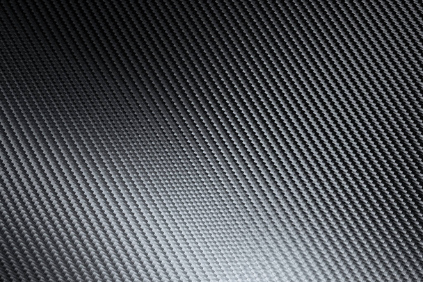 Strukturelles Detail einer industriellen Kohlefaserplatte in einer Vollrahmenansicht, die das sich wiederholende diagonale Muster zeigt, während das Licht in einer Hintergrundstruktur über die Oberfläche spielt - Foto, Bild
