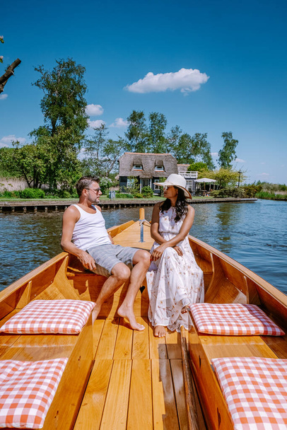 Giethoorn Netherlands couple visit the village with a boat ,view of famous village with canals and rustic thatched roof houses in farm area on a hot Spring day - Foto, Bild