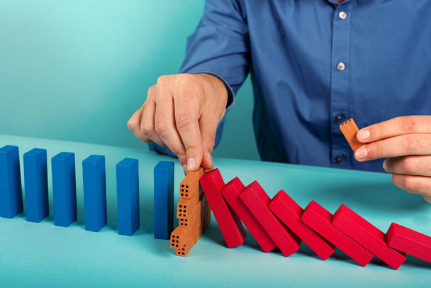 Businessman stops a chain fall like domino game. Concept of preventing crisis and failure in business. - Photo, Image