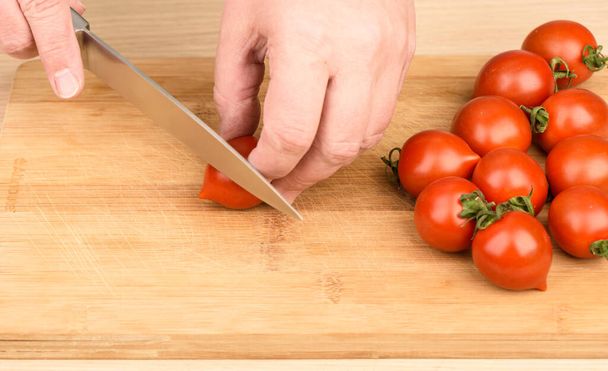 Slicing cherry tomatoes on a cutting board. Woman cuts cherry tomatoes with a knife. Close up. - Φωτογραφία, εικόνα