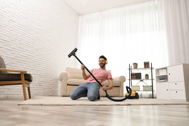 Young man having fun while vacuuming at home - Foto, Bild