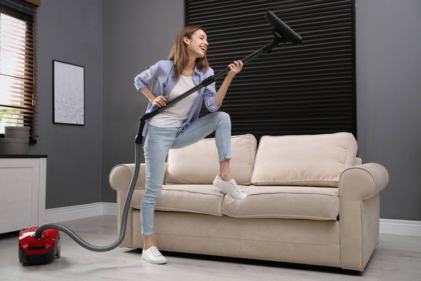 Young woman having fun while vacuuming at home - Foto, imagen