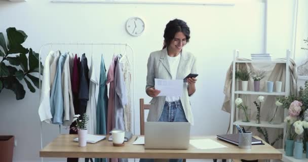 Smiling young female fashion designer using smart phone at workplace - Séquence, vidéo