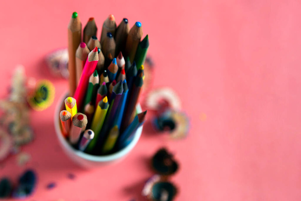 Egy halom színes ceruza és borotválkozás körülötte. Fa ceruza forgács rózsaszín pasztell papír háttér. Első látásra. Tervezési elemek plakát, banner, kártyák - Fotó, kép
