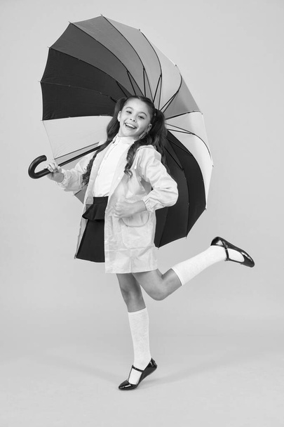 autumn fashion for kids. small girl feel comfortable under umbrella. happy child with colorful umbrella. cheerful school girl in trendy raincoat. ready for autumn rainy weather - Fotó, kép