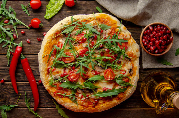 Vegan pizza with fresh garnet and arugula leaves on old wooden background - Foto, Imagem