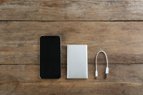 Mobile phone and portable charger on wooden background, flat lay - 写真・画像
