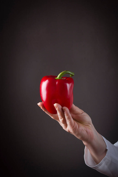 Female hand with bell pepper on a black background - Foto, Bild