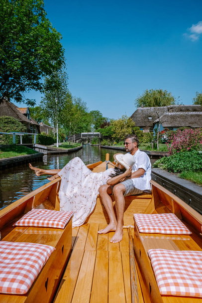Giethoorn Netherlands couple visit the village with a boat ,view of famous village with canals and rustic thatched roof houses in farm area on a hot Spring day - Valokuva, kuva