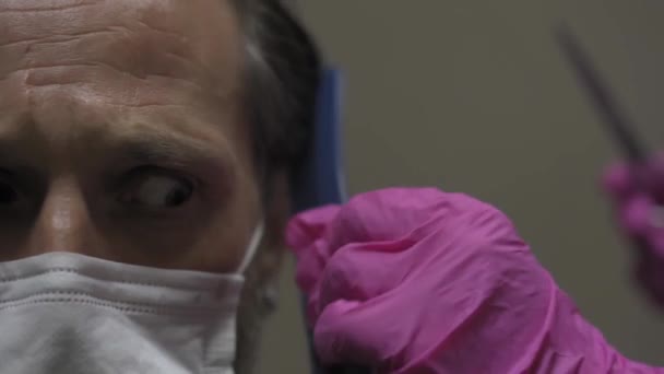 A frightened man in a protective mask sits at the hairdresser on a haircut, looks incredulously to the side. Close up. Barber quarantine. Prores 422 - Materiał filmowy, wideo