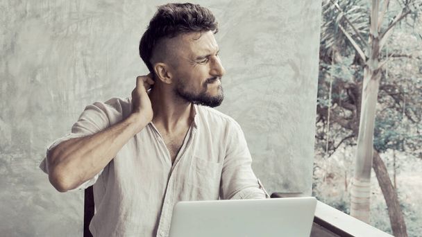 Um homem que sofre de dor nas costas do pescoço, em seguida, trabalhou no laptop e olhando sobrecarregado e estressante
 - Foto, Imagem