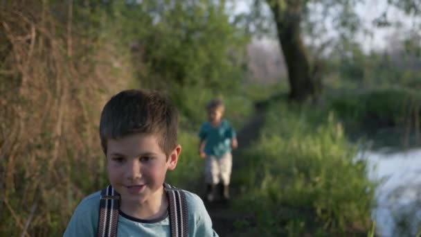 mannelijke kinderen lopen elkaar achterna op de weg langs de rivier - Video
