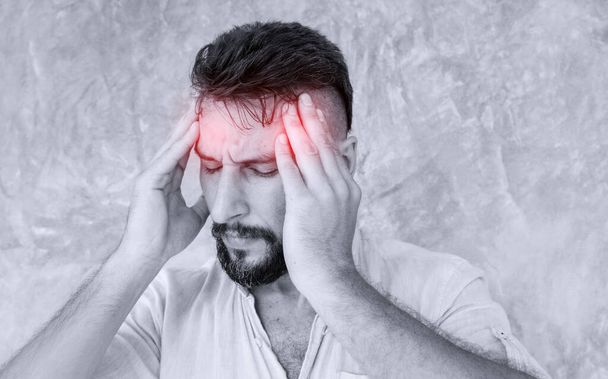 Ένας άντρας που υποφέρει από πονοκέφαλο από πόνο στο κεφάλι και δείχνει κουρασμένος, ανήσυχος και αγχωμένος. - Φωτογραφία, εικόνα