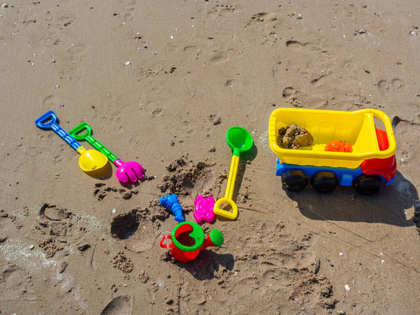 Colorful children's beach toys, green with shovel, truck and shower mug on wet sand on the beach background. - Photo, Image