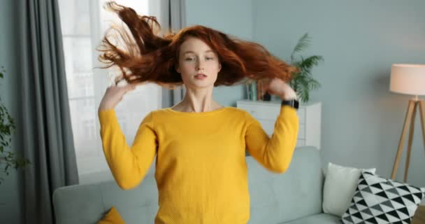 Portrait of young Caucasian red-haired woman smiling in cozy living room. Beautiful styllish girl with red curly hair looking at camera like in mirror. Indoor. At home. - Video